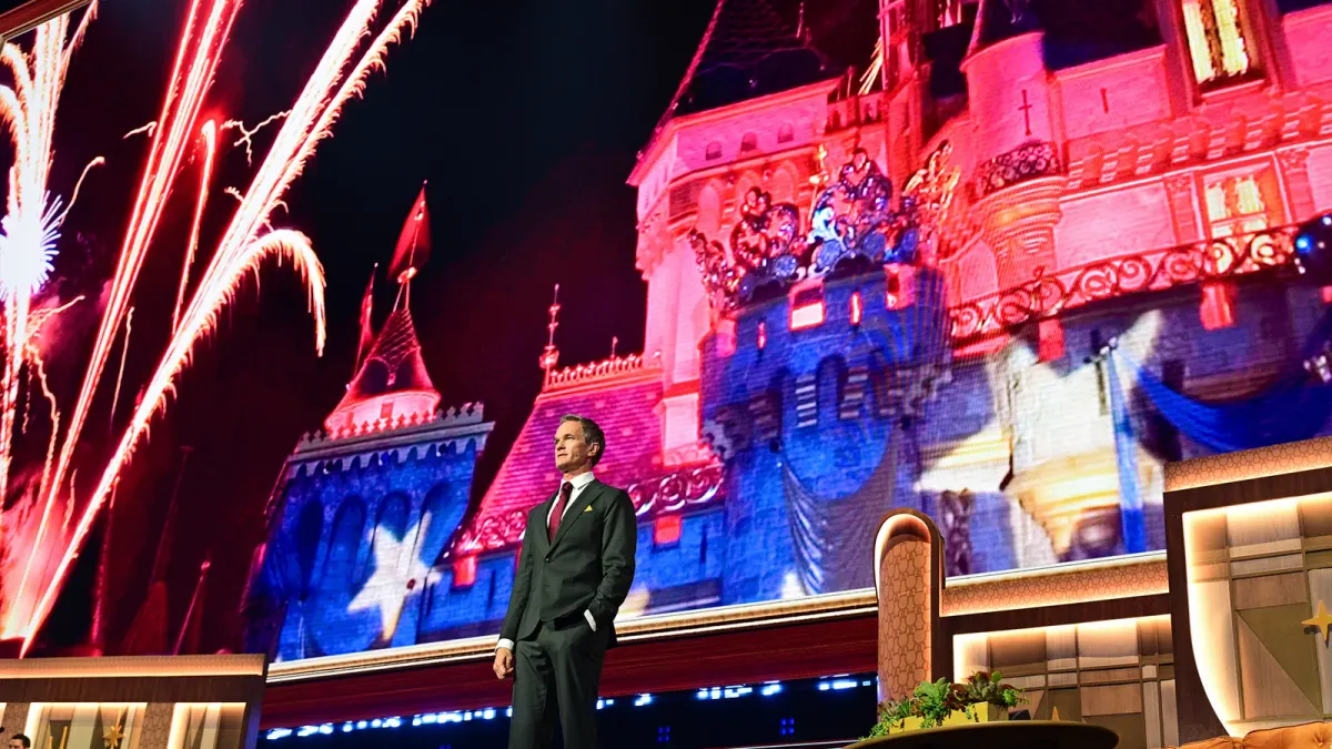 Neil Patrick Harris stands onstage at Disney's August 15 Horizons showcase with Disneyland imagery projected behind him