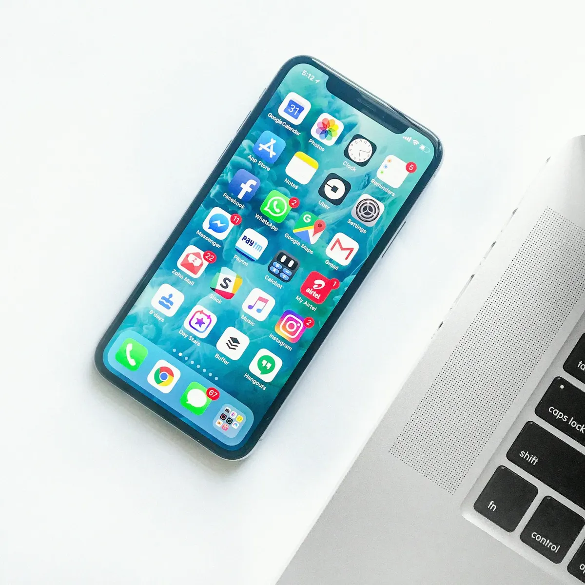 An iPhone displaying app icons rests beside a laptop on a white desk