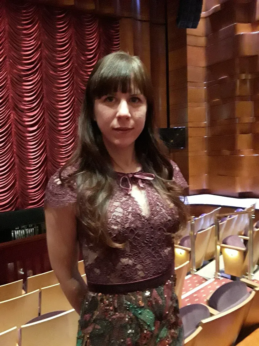 Composer Missy Mazzoli standing inside an auditorium with red curtains