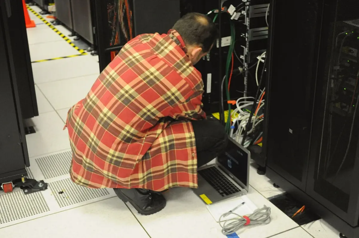 Technician kneeling with a laptop while working on a server rack