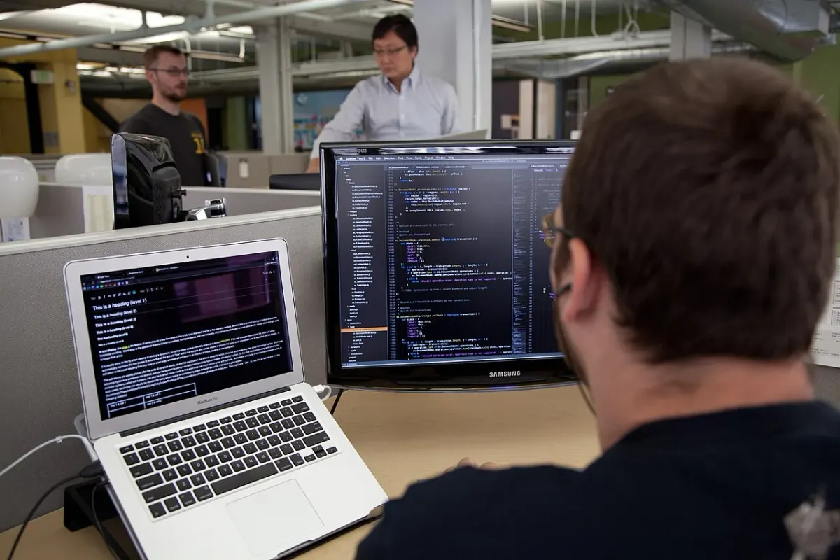 Developer seated in front of a laptop and a larger monitor showing code