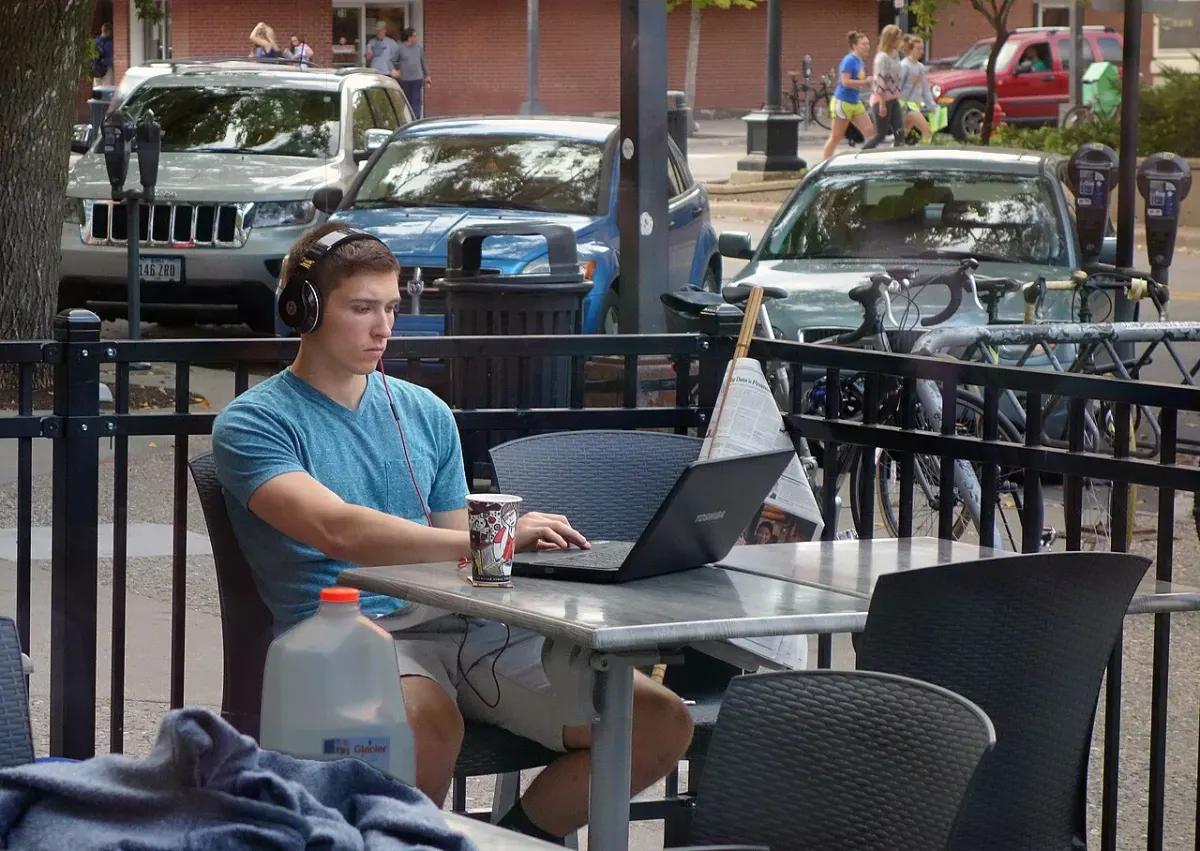 Person using a laptop at an outdoor cafe table beside a street