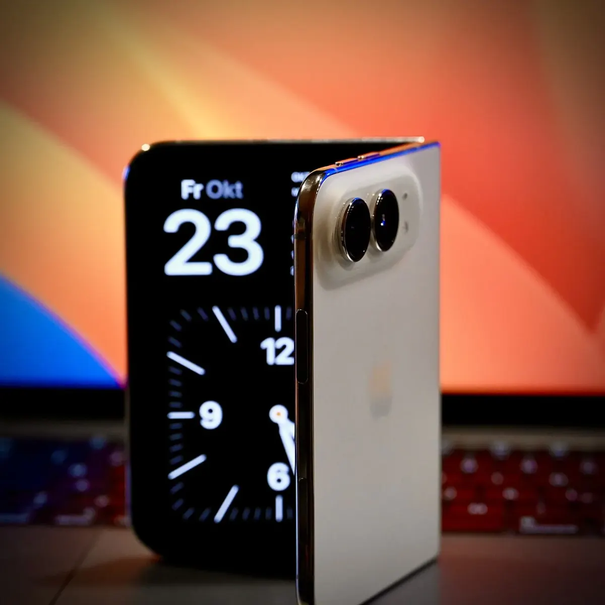 Partly folded iPhone Duo on a desk with a laptop behind it