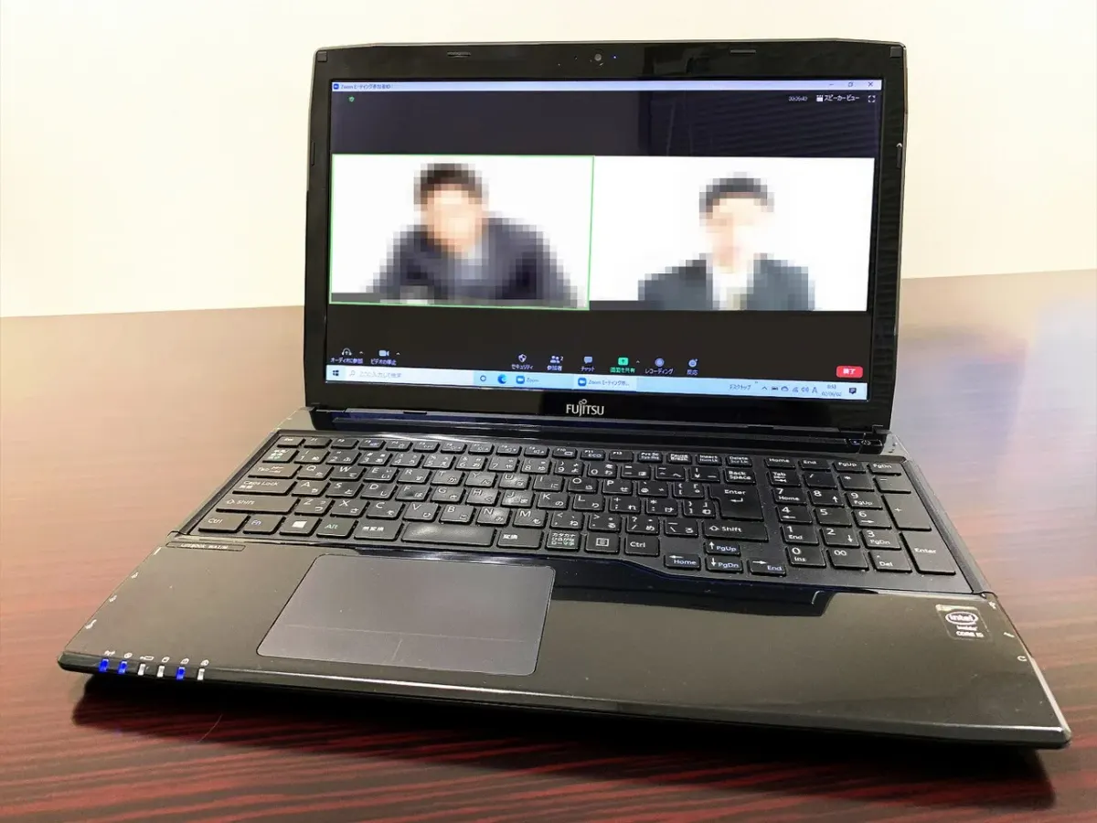 Laptop on a wooden table displaying two participants in a video call