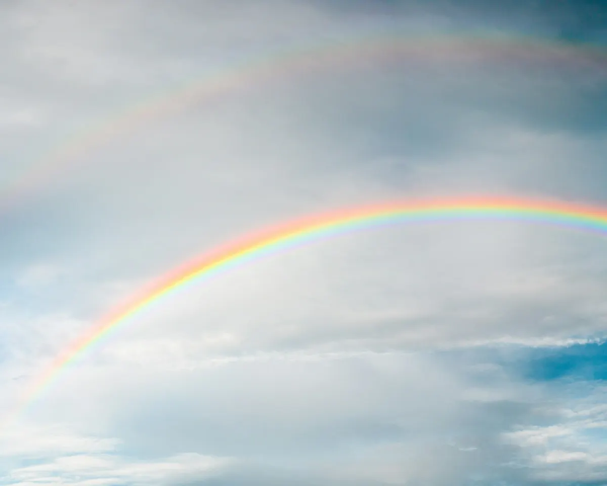 A bright rainbow curving across a gray-blue cloudy sky