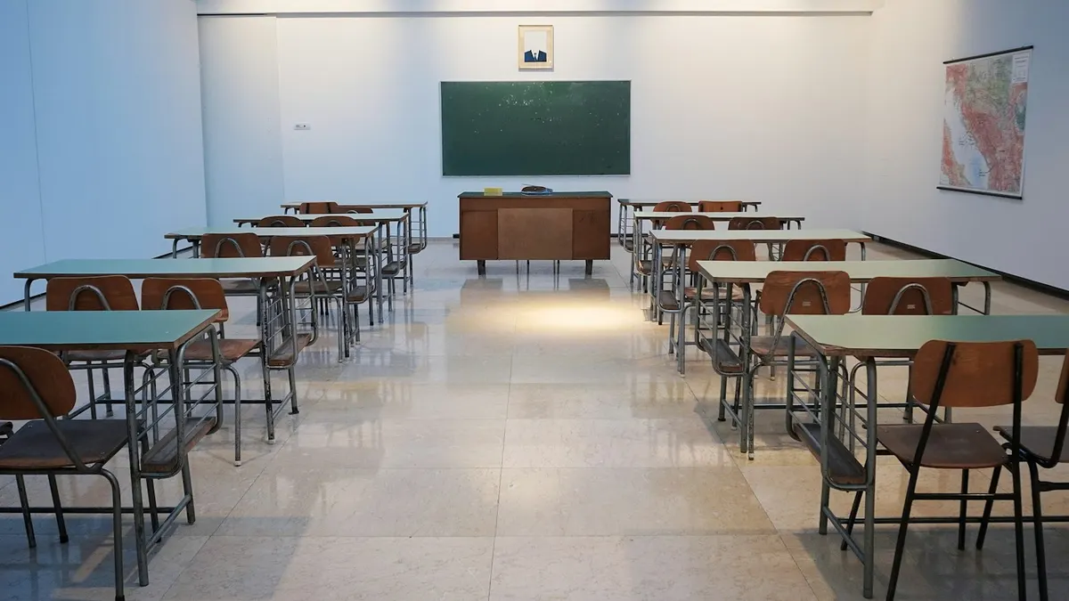 Rows of empty classroom desks facing a green chalkboard