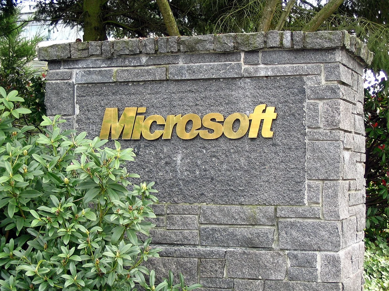 A stone sign with the Microsoft name in gold letters beside green shrubs