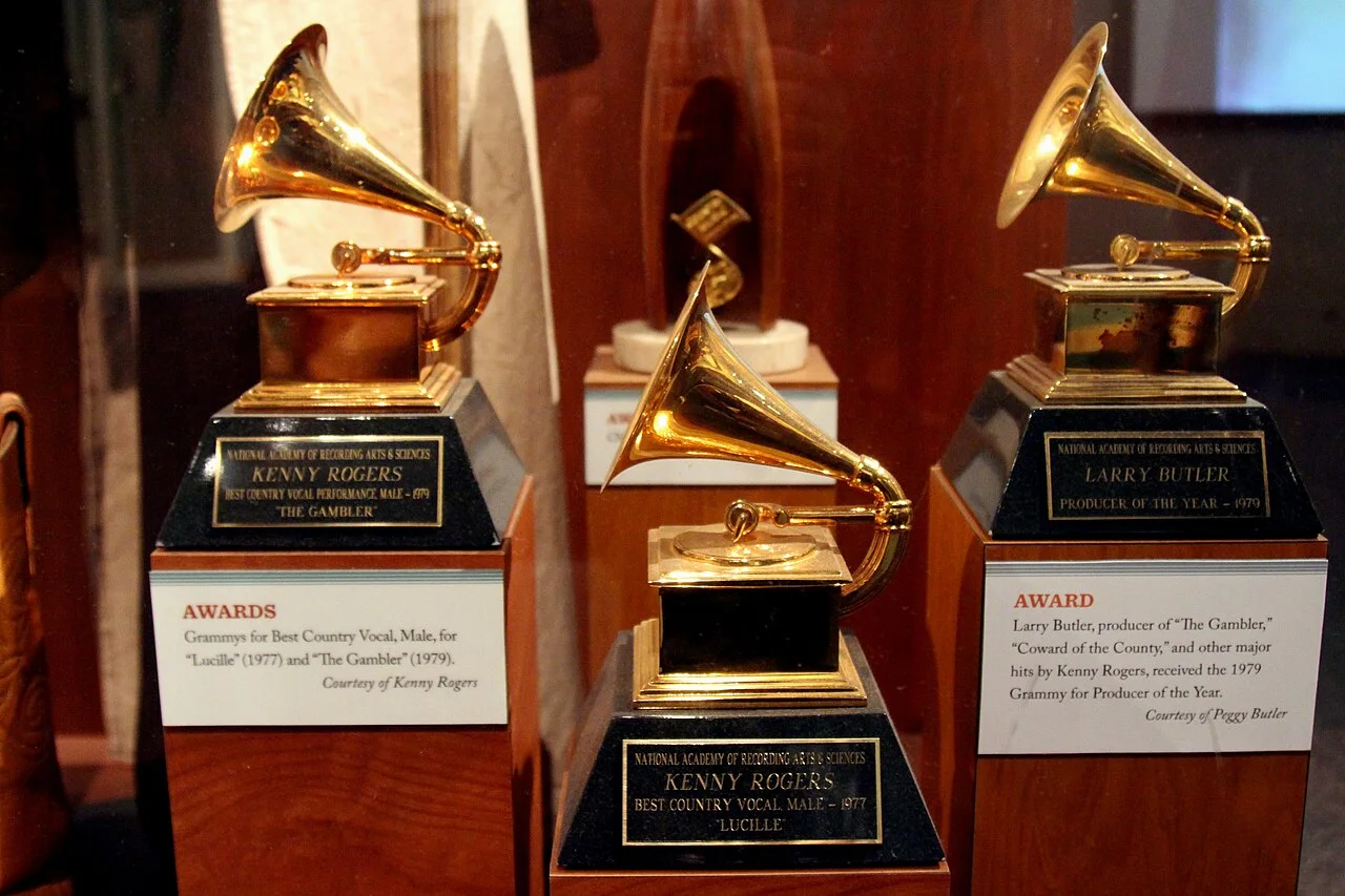Three gold gramophone-shaped Grammy statuettes on wooden bases in a museum display case with award placards