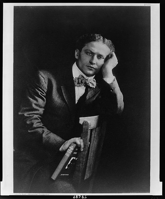 Harry Houdini seated with a copy of The Unmasking of Robert-Houdin, resting his head on one hand