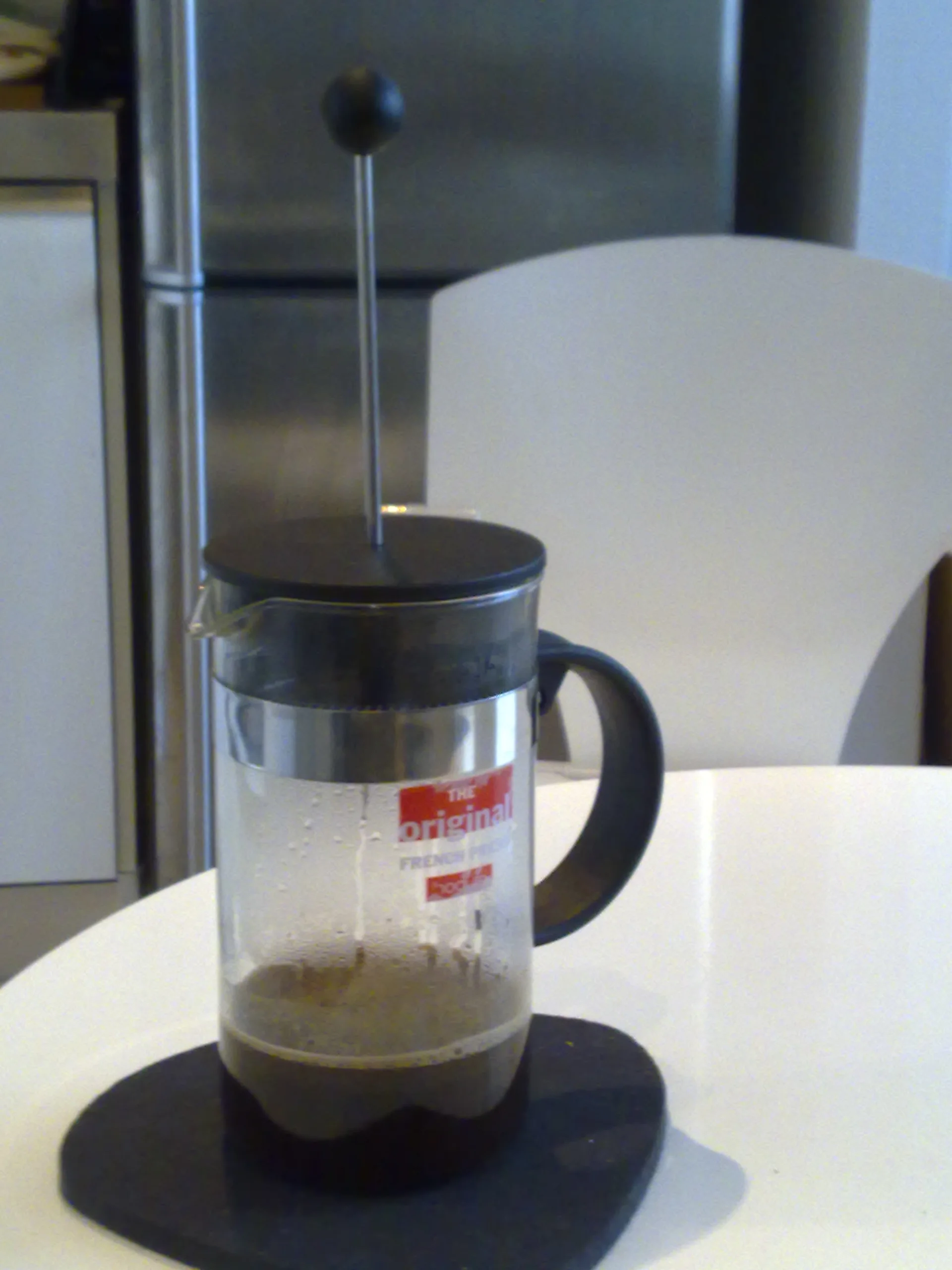 A Bodum French press containing coffee stands on a round black mat in a kitchen.