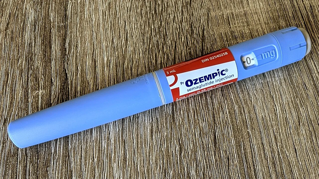 A blue Ozempic semaglutide injection pen with a red label lying on a wooden table