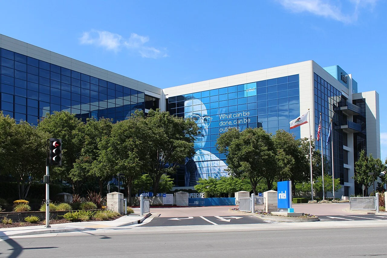 Intel's glass-walled headquarters building in Santa Clara, California, with an Intel sign out front and a large poster on the facade