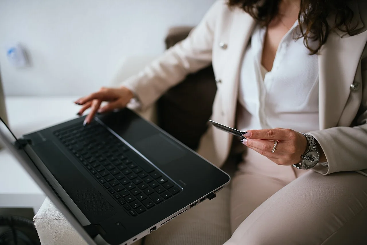 A person holding a payment card beside an open laptop