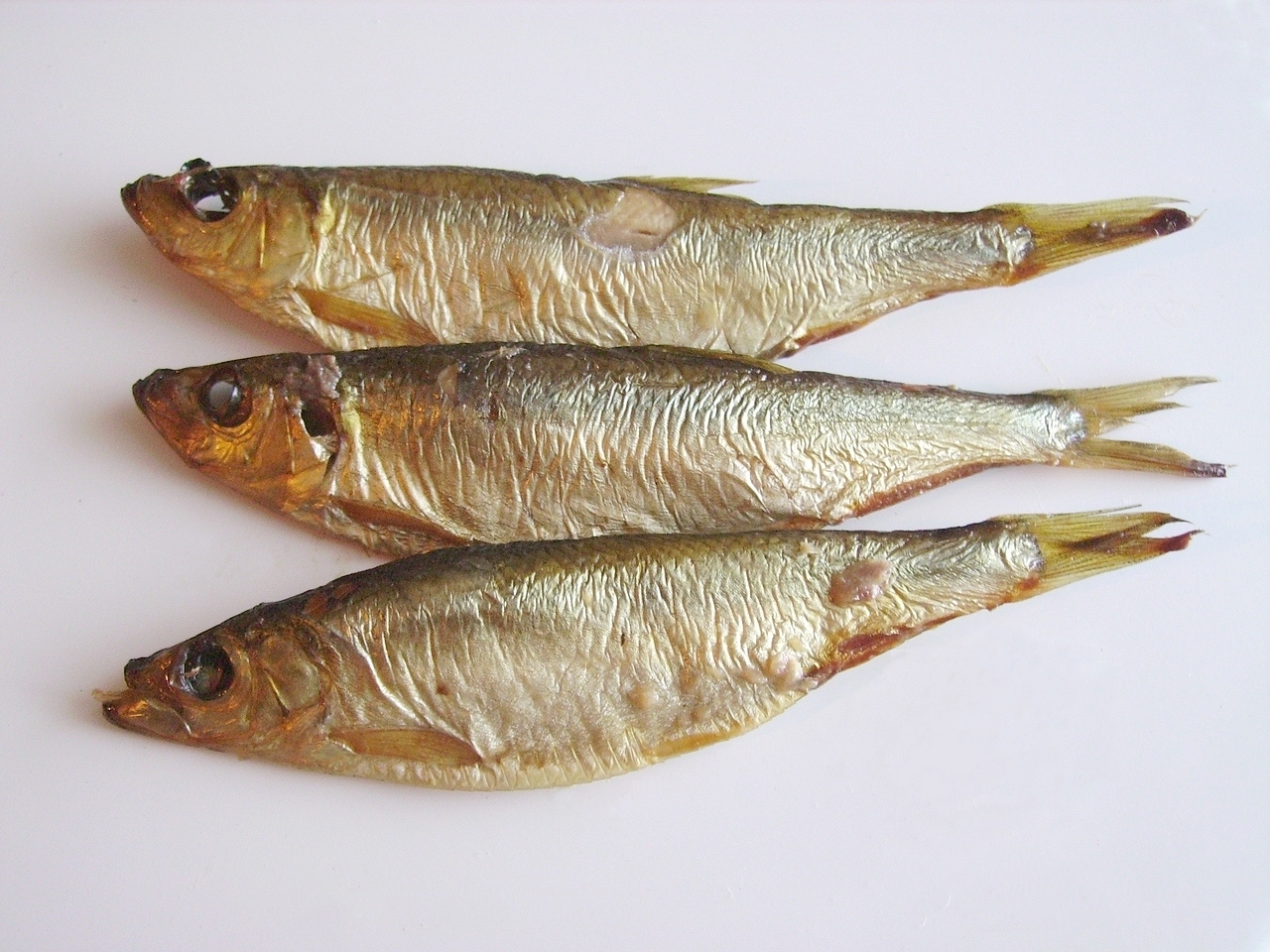 Three whole smoked European sprats on a white surface in an archival photograph.
