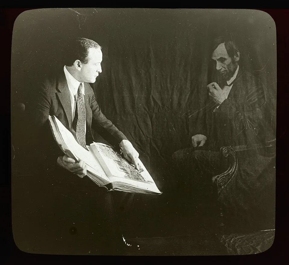 Houdini seated with an open book beside a translucent image of Abraham Lincoln