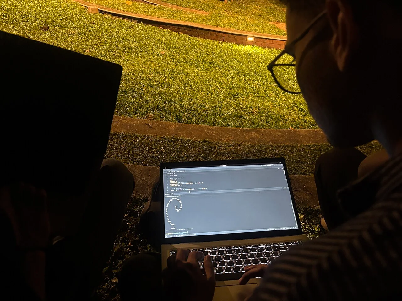 A participant works on a Python script on a laptop at an outdoor Debian event.
