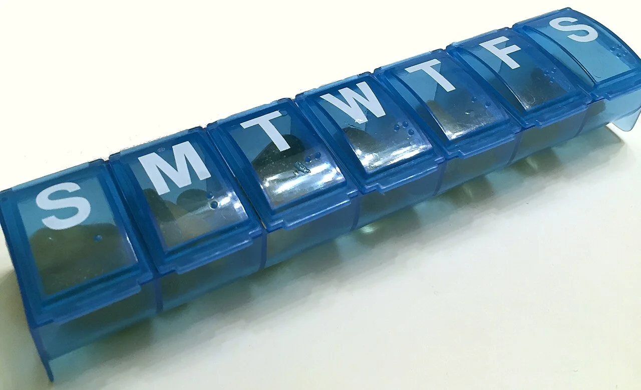 A blue weekly pill organizer with compartments labeled by day