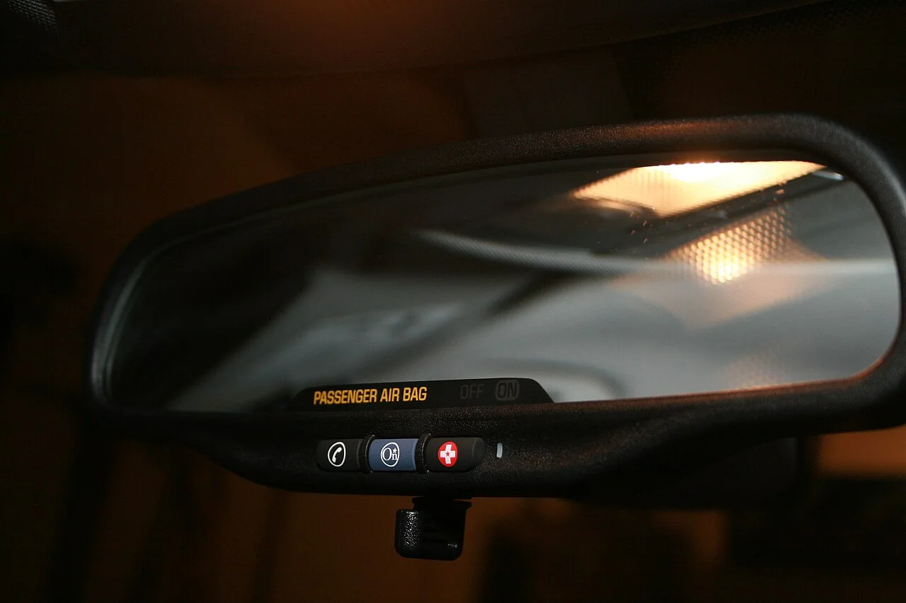 A car rearview mirror with three OnStar buttons along its lower edge, lit in a dark cabin