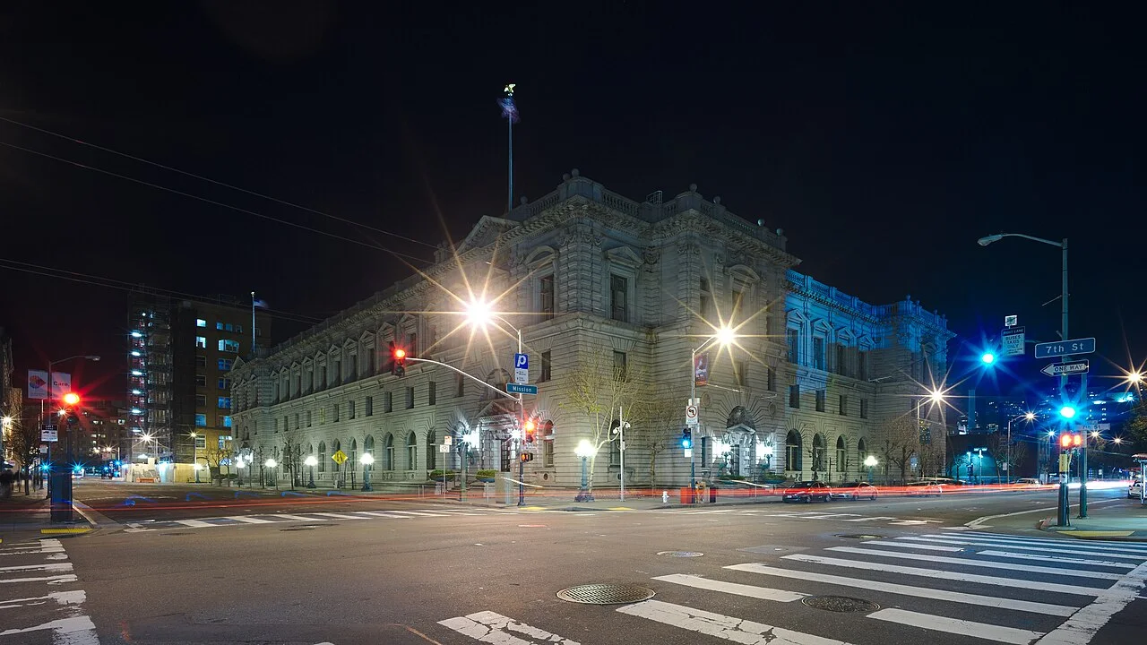 A large Beaux-Arts stone courthouse lit up at night on a San Francisco street corner