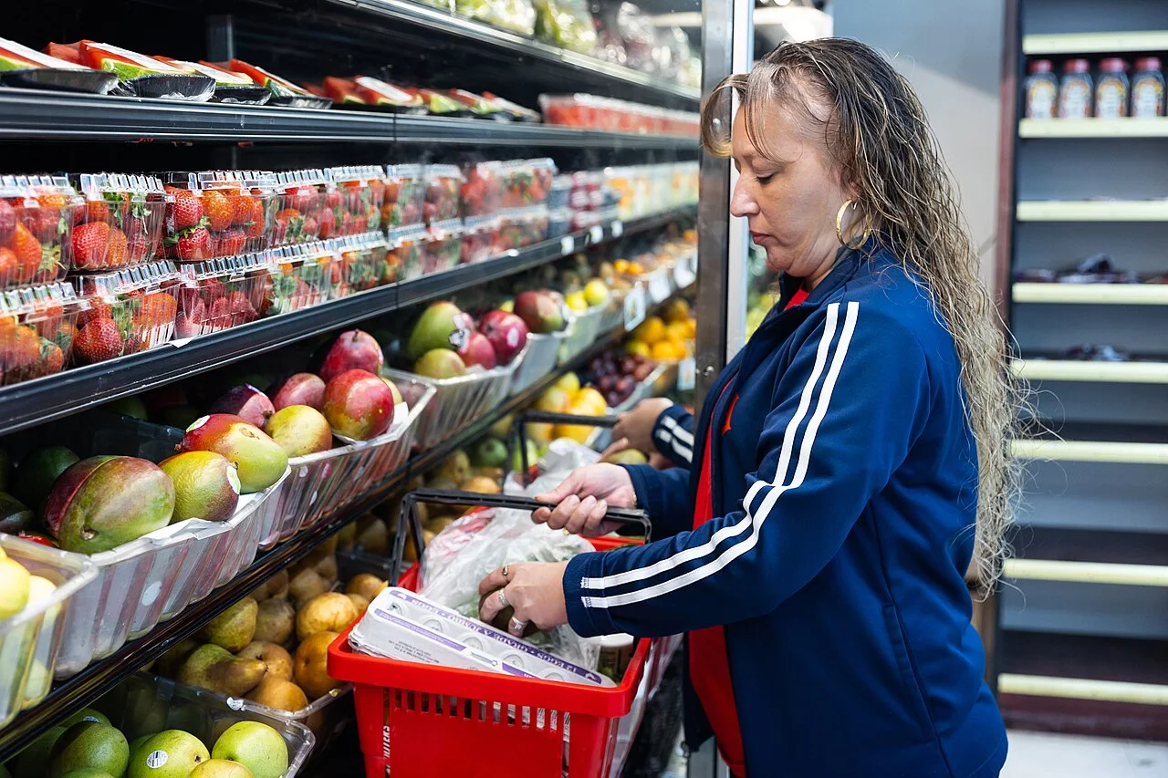 A shopper with a red basket stands beside mangoes and other fresh produce in a Detroit grocery store.
