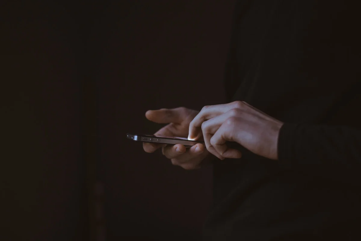 Hands holding and using a smartphone against a dark background