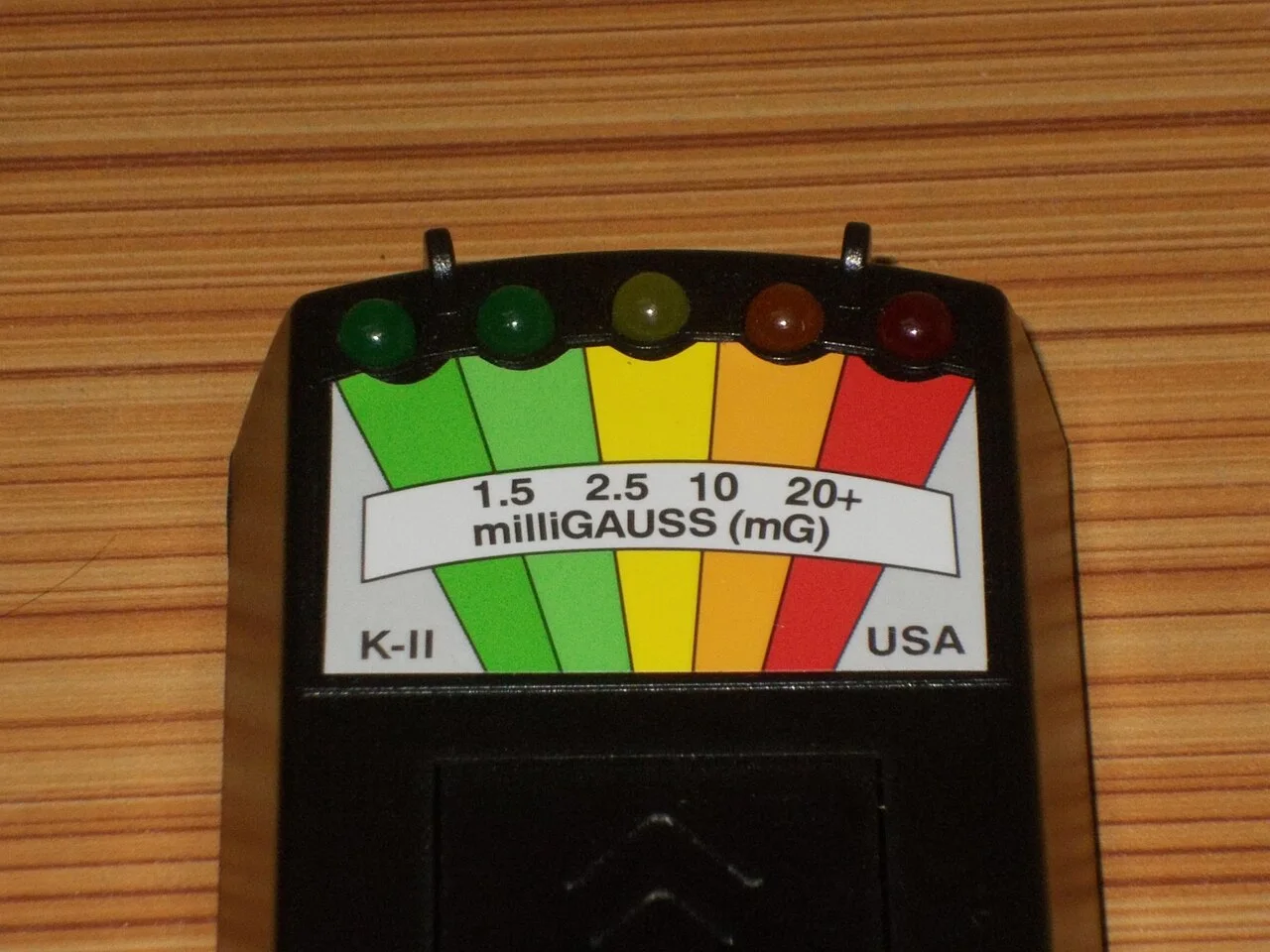 A K-II electromagnetic-field meter with a colored milligauss scale on a wooden surface.