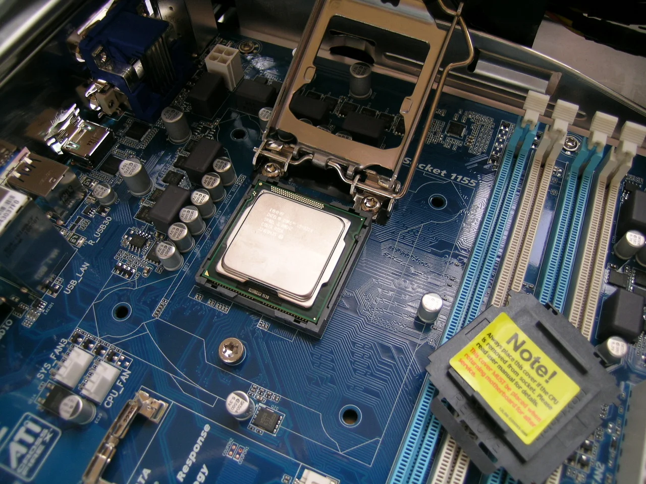 An Intel desktop processor seated in the open socket of a blue computer motherboard, with memory slots and capacitors around it