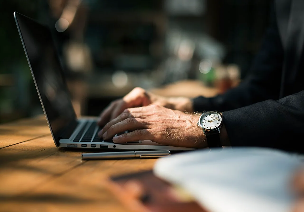 Hands typing on a laptop at a wooden table