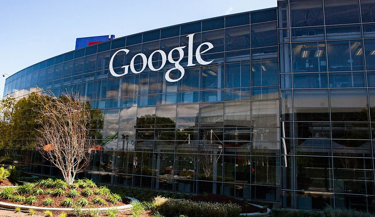 A curved glass office building with a large white Google logo at the company headquarters