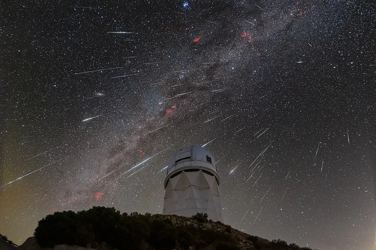 Dozens of meteor streaks and the Milky Way over a white telescope dome on a dark hilltop